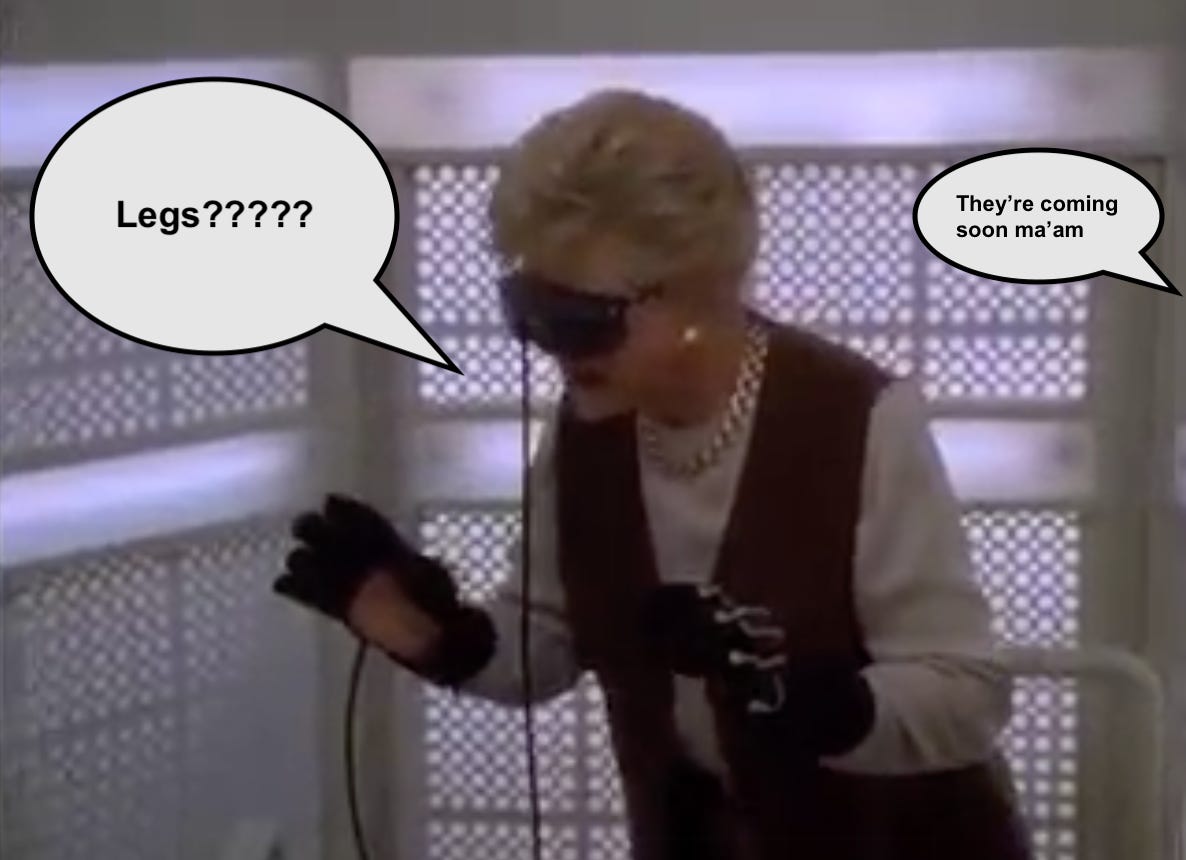 A screengrab from the 1993 Murder, She Wrote episode “A Virtual Murder” showing Angela Lansbury’s Jessica Fletcher in VR gloves and goggles. She is saying “Legs?????” while from offscreen someone answers “They’re coming soon ma’am”