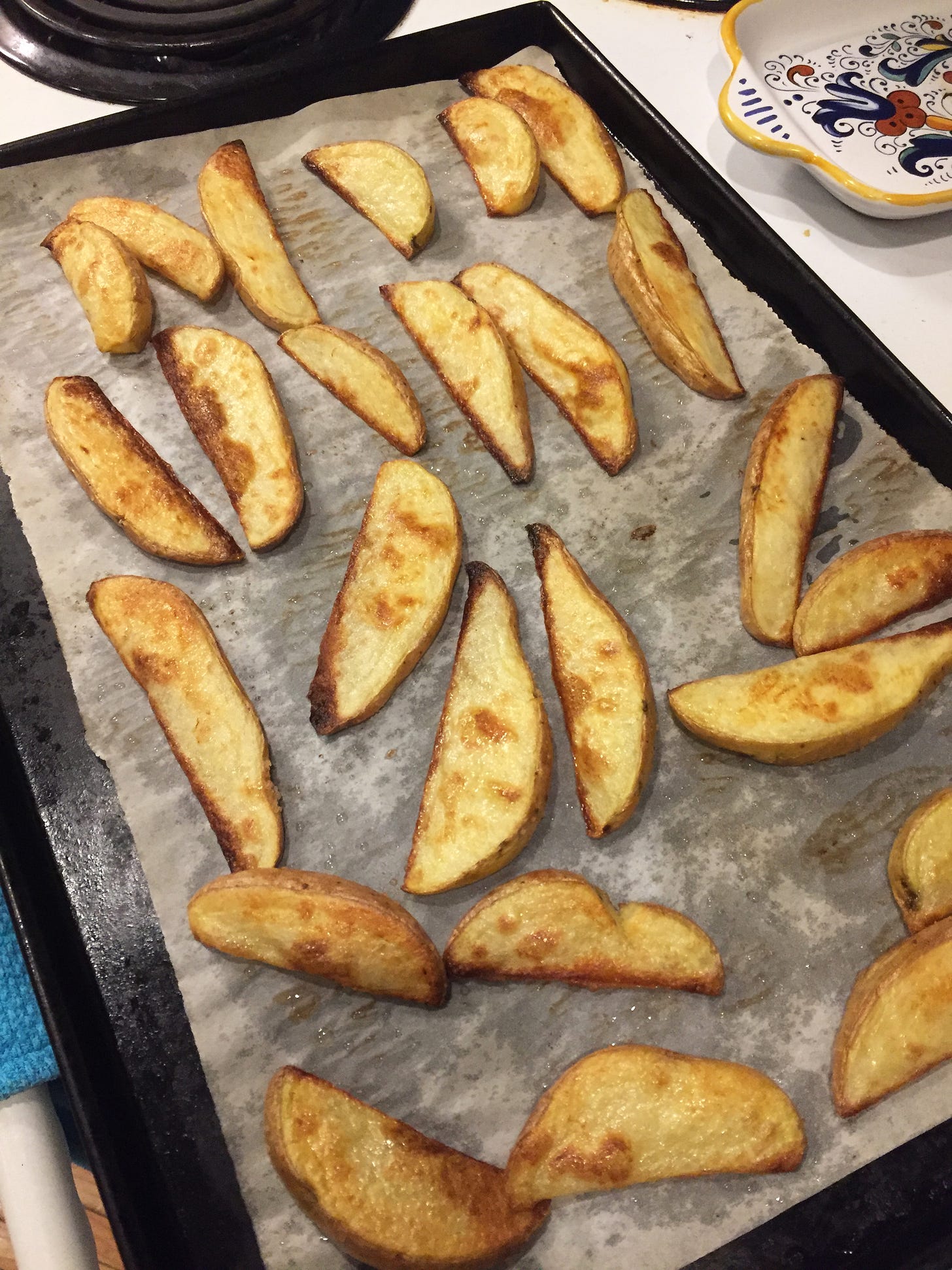 A baking sheet lined with parchment and sitting on top of the stove, full of perfectly browned wedge fries.