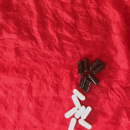 A stop-motion photo animation loop of a red background with equally-sized black pills and white pills that dance around together and then march offscreen.