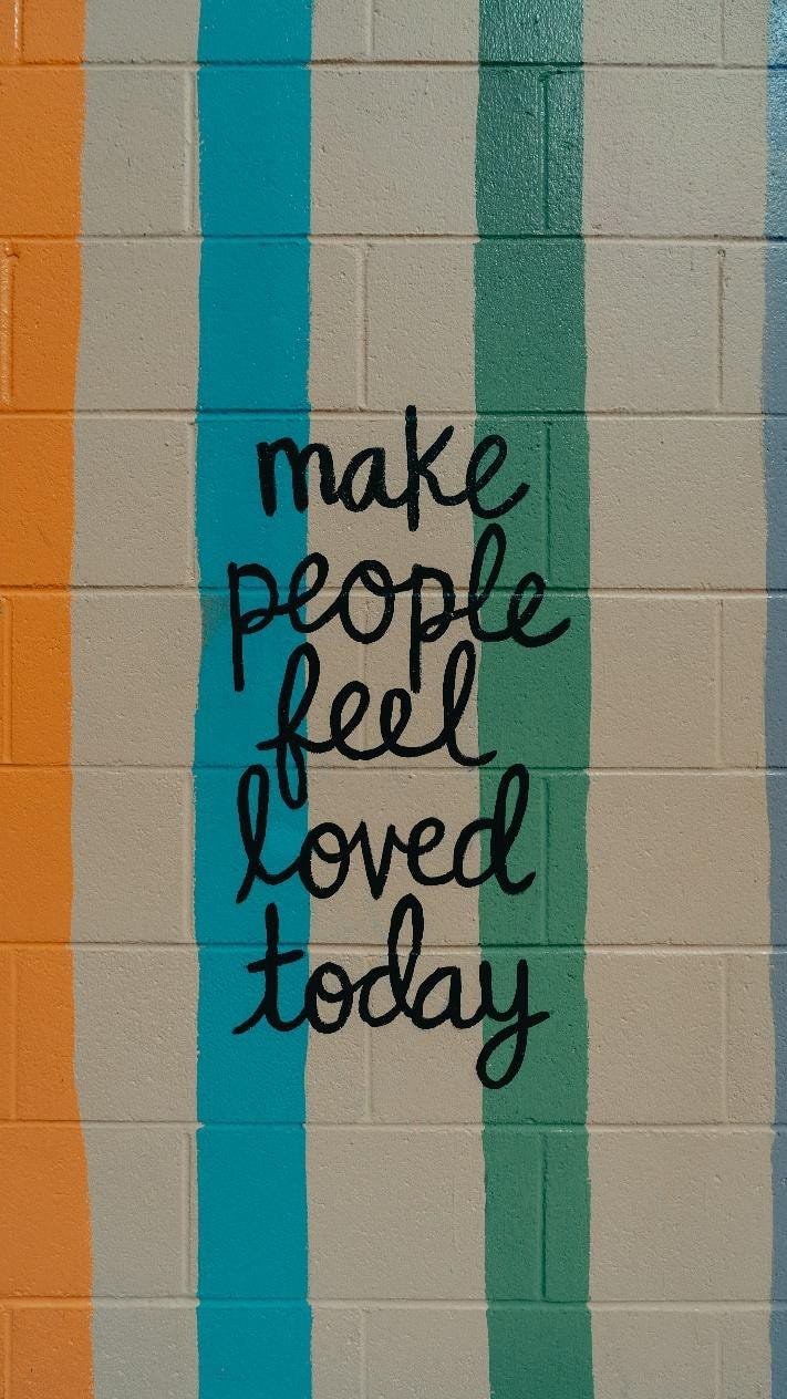 Graffiti on colourful stripped wall, reads “make people feel loved today”.