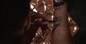 John McClane's wrist showing the number 6 as a tally and the names 'Hans' and 'Karl' written in Sharpie