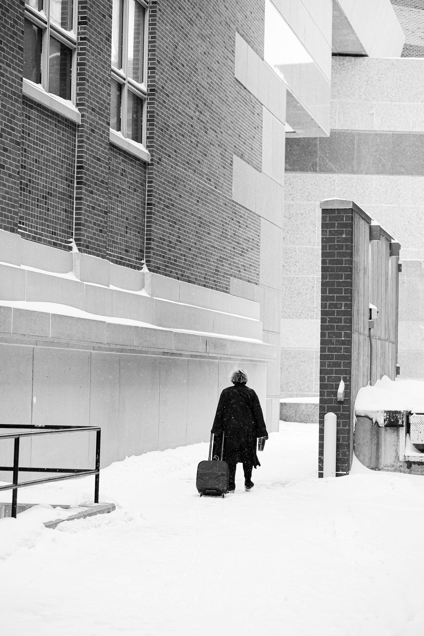 A woman drags her rolling suitcase down the snowy path. 