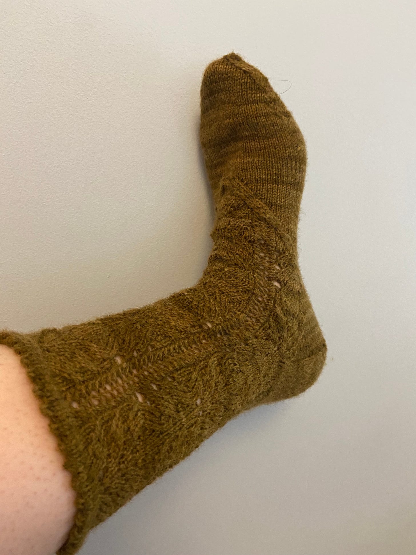 a dusty green hand knit sock with a lacy pattern