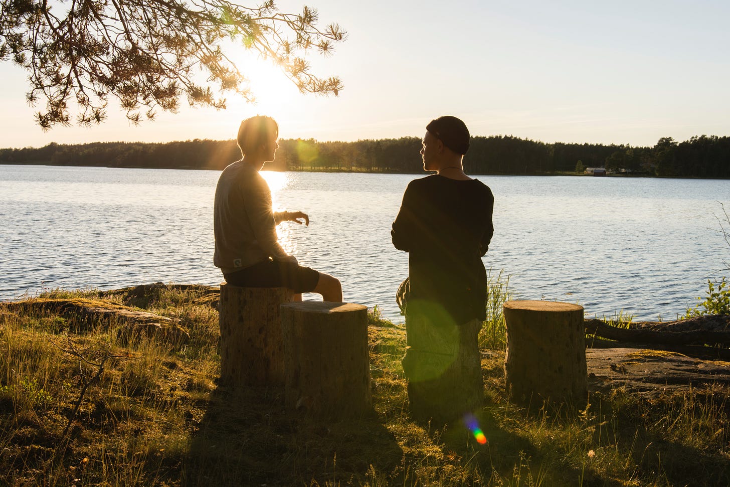 Two men sitting next to a lake talking.