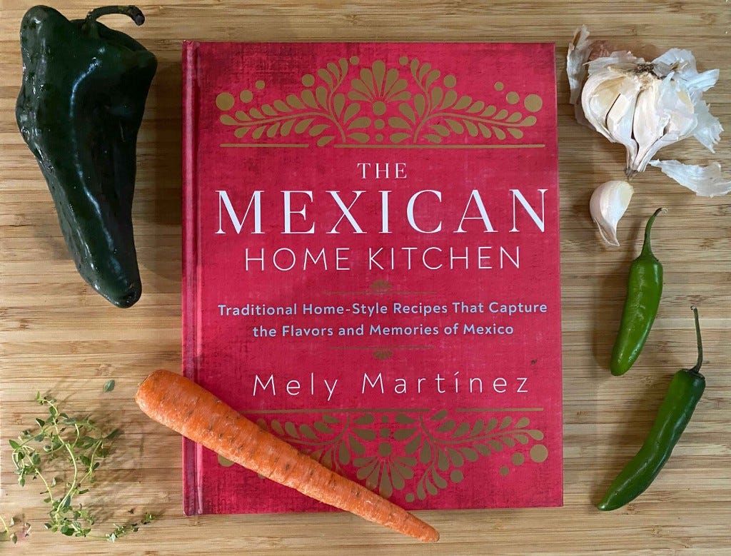 ‘The Mexican Home Kitchen’ cookbook, shown on a bamboo cutting board with fresh chiles, garlic, thyme and a carrot