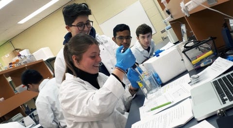 students in lab coats pipetting at a bench