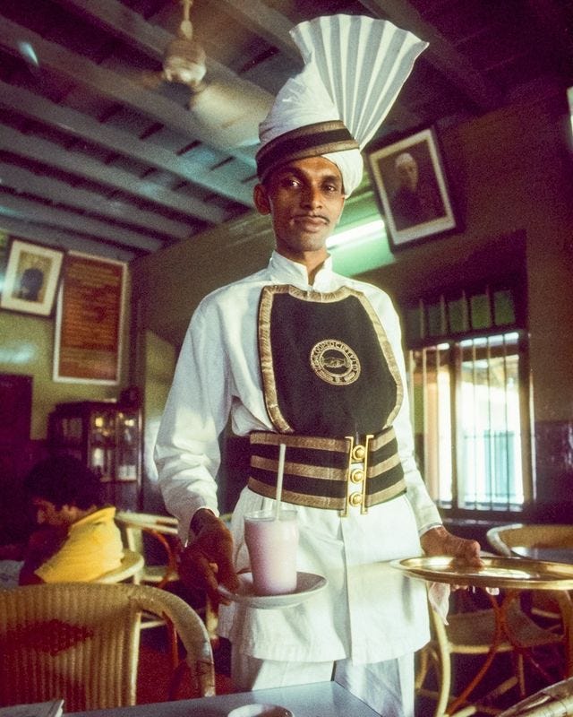 At a coffee house in Kerala, India, the traditionally garbed server brings a rose-water lassi, or yogurt drink. Overhead the fans try to keep things cool. - Kevin Kelly