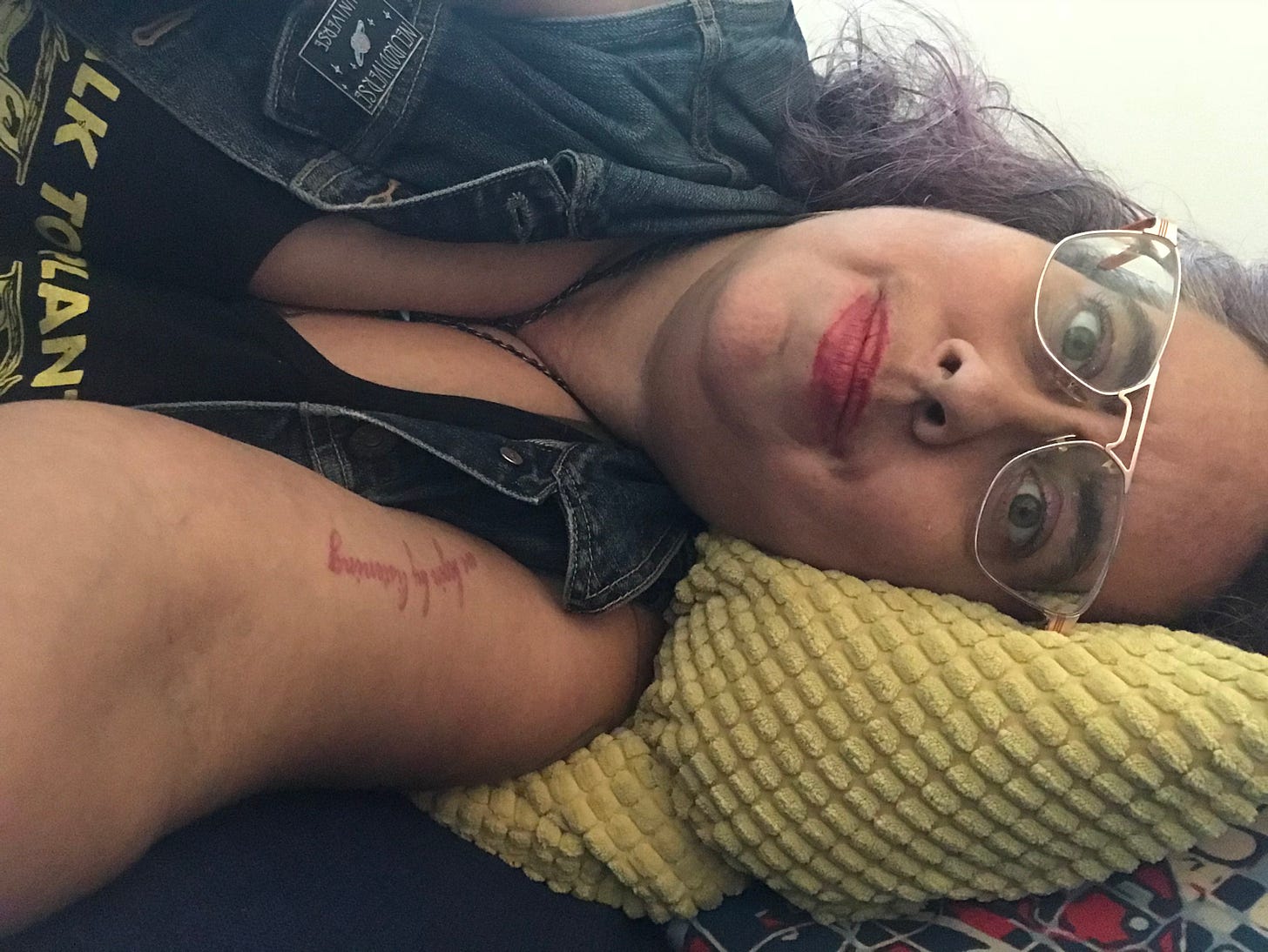Photograph of author Leah Lakshmi Piepzna-Samarasinha, light sand skinned non-binary femme, wearing glasses and laying on her side on a green pillow.   