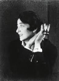 Black and white photo of Eileen Gray. She is looking off to the side and smiling, with her hands up by her face. 