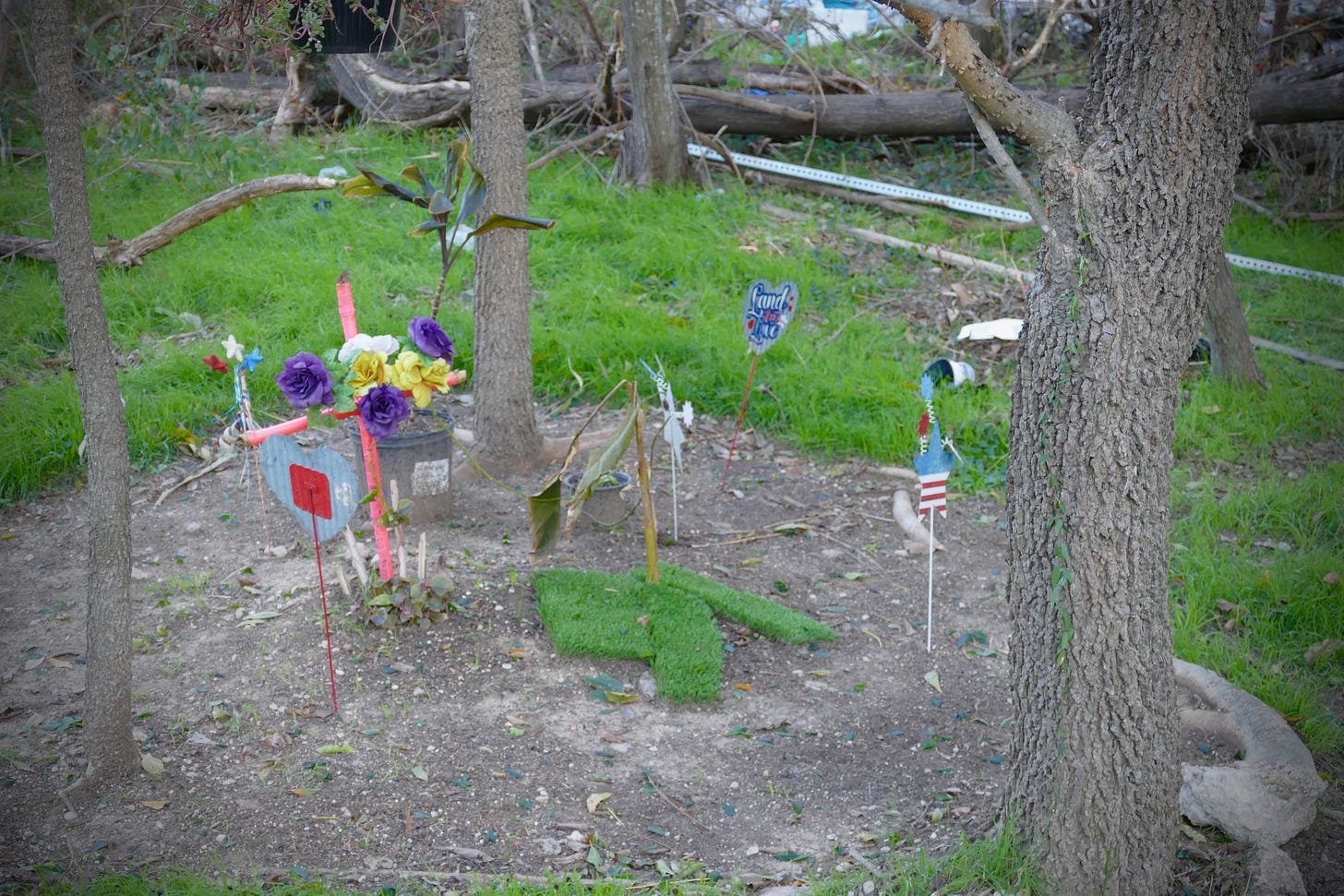 Picture of a shrine with pink cross and other decorations in the heart of a homeless camp, as described in more detail in the paragraph that follows