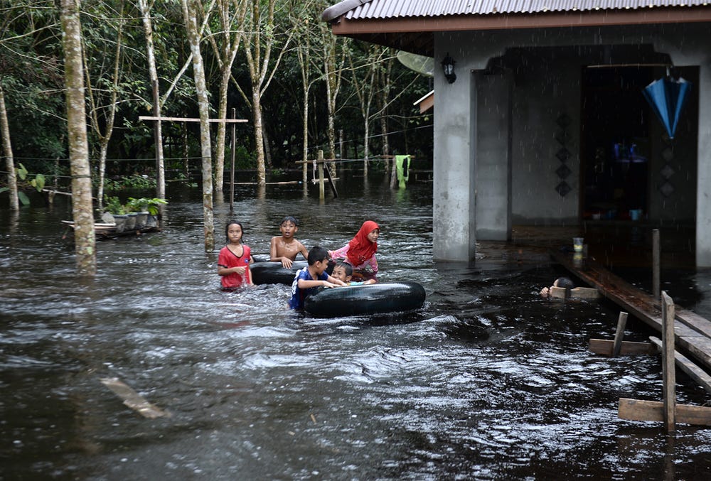Children play outside a house affected by floodwaters following heavy rains in southern Thai province of Narathiwat on 2 December 2019.