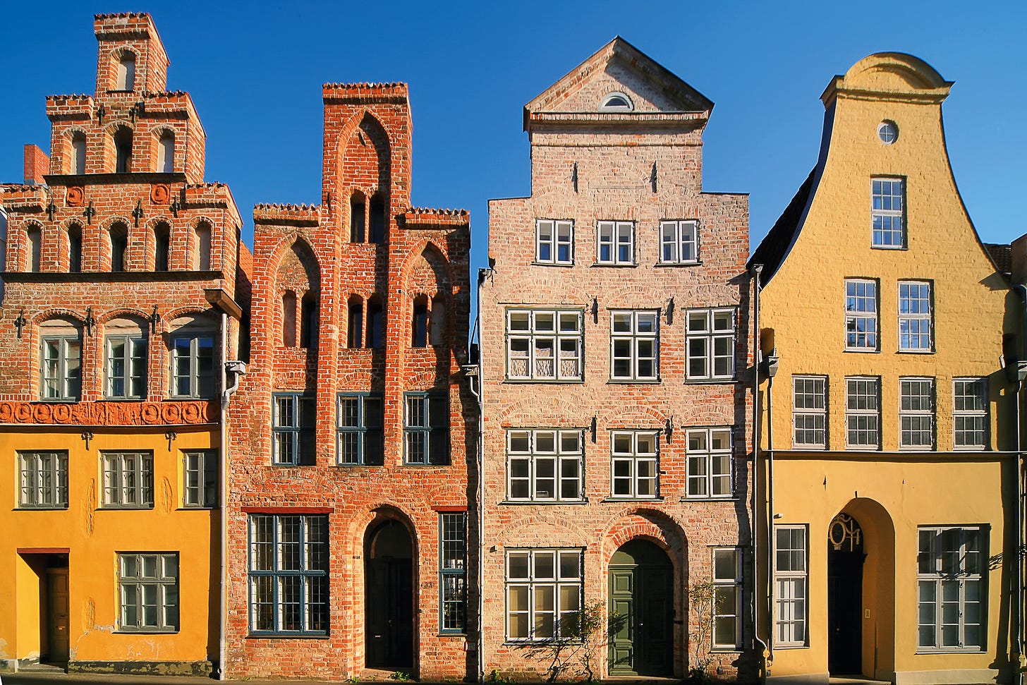 A row of four very old, tall, gabled houses in reds and yellows