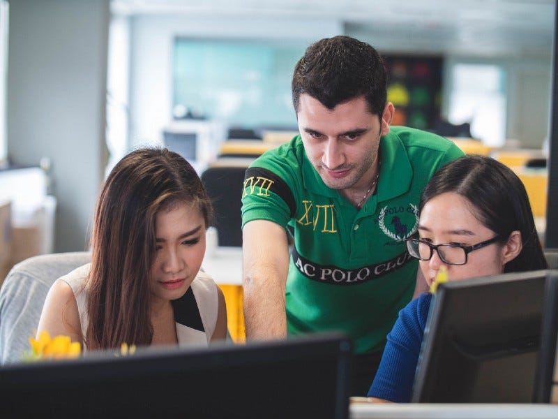 A man explaining something to two Asian girls in front of a computer