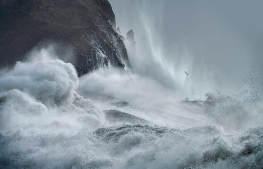 Ocean waves smash up against a rocky cliff.