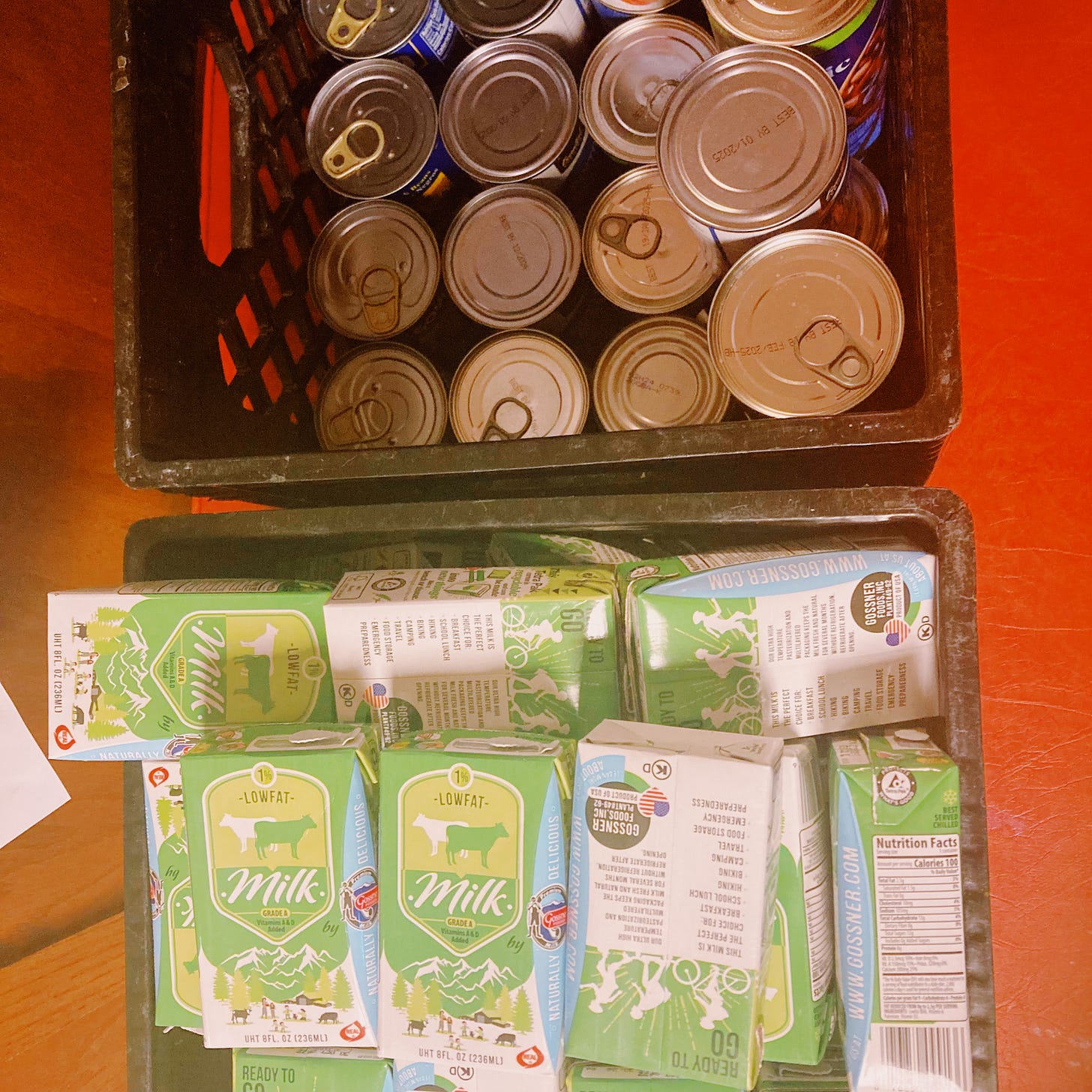 two black crates are filled with food cans and green milk cartons