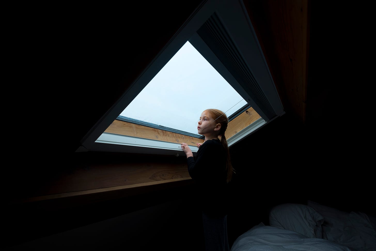 A young girl with red hair peers out of a skylight window in an A Frame bedroom