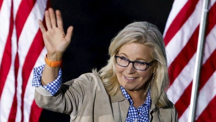 Liz Cheney waves in front of American flags in Jackson, Wyoming on Tuesday