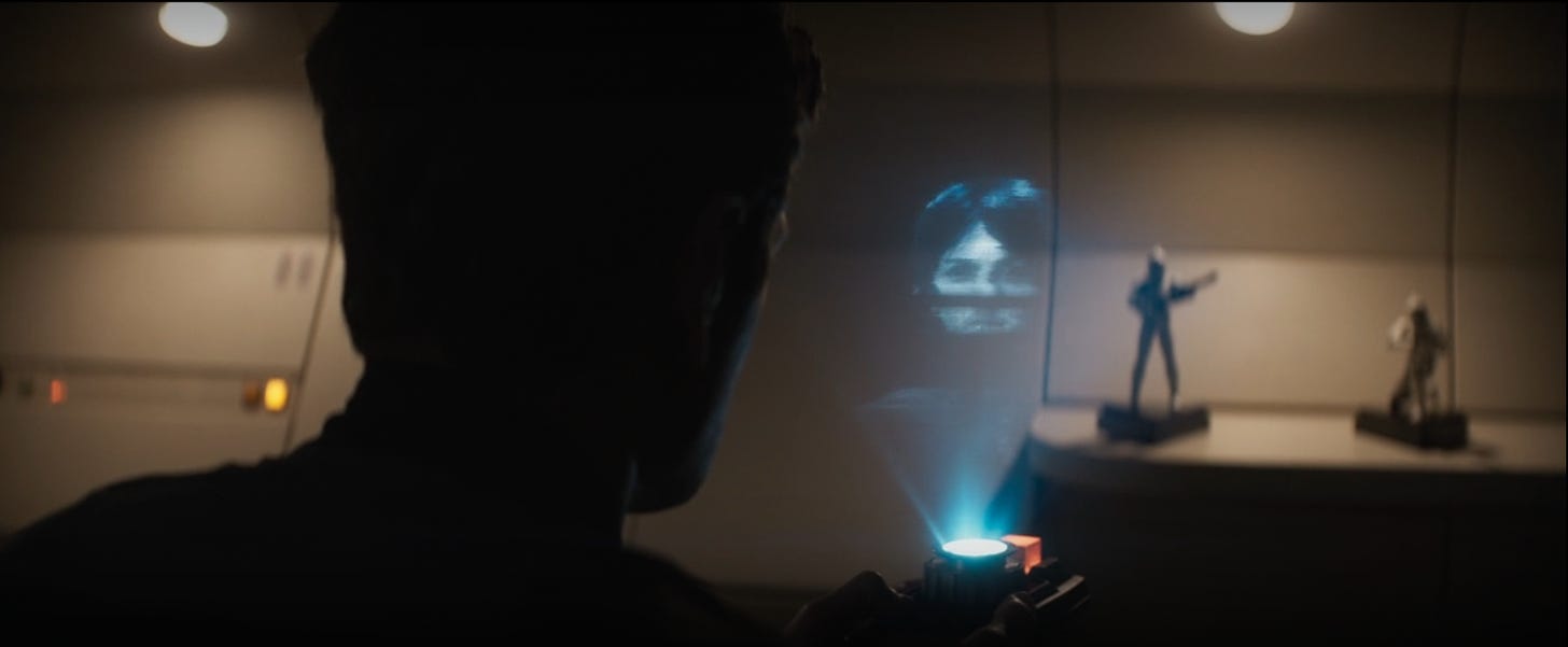 Cyril Karn looks at a hologram of Cassian Andor while his action figures watch. 