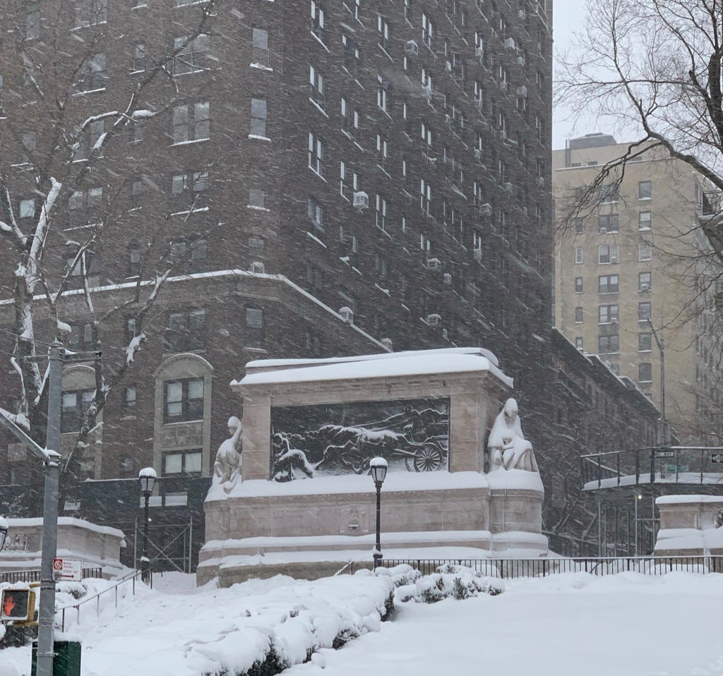 Photo is the Firemen's memorial (a large stone monument with a bronze relief plaque) on Riverside Drive, covered in snow, which accentuates the team of horses on the bronze plaque, as snow continues to fall all around.