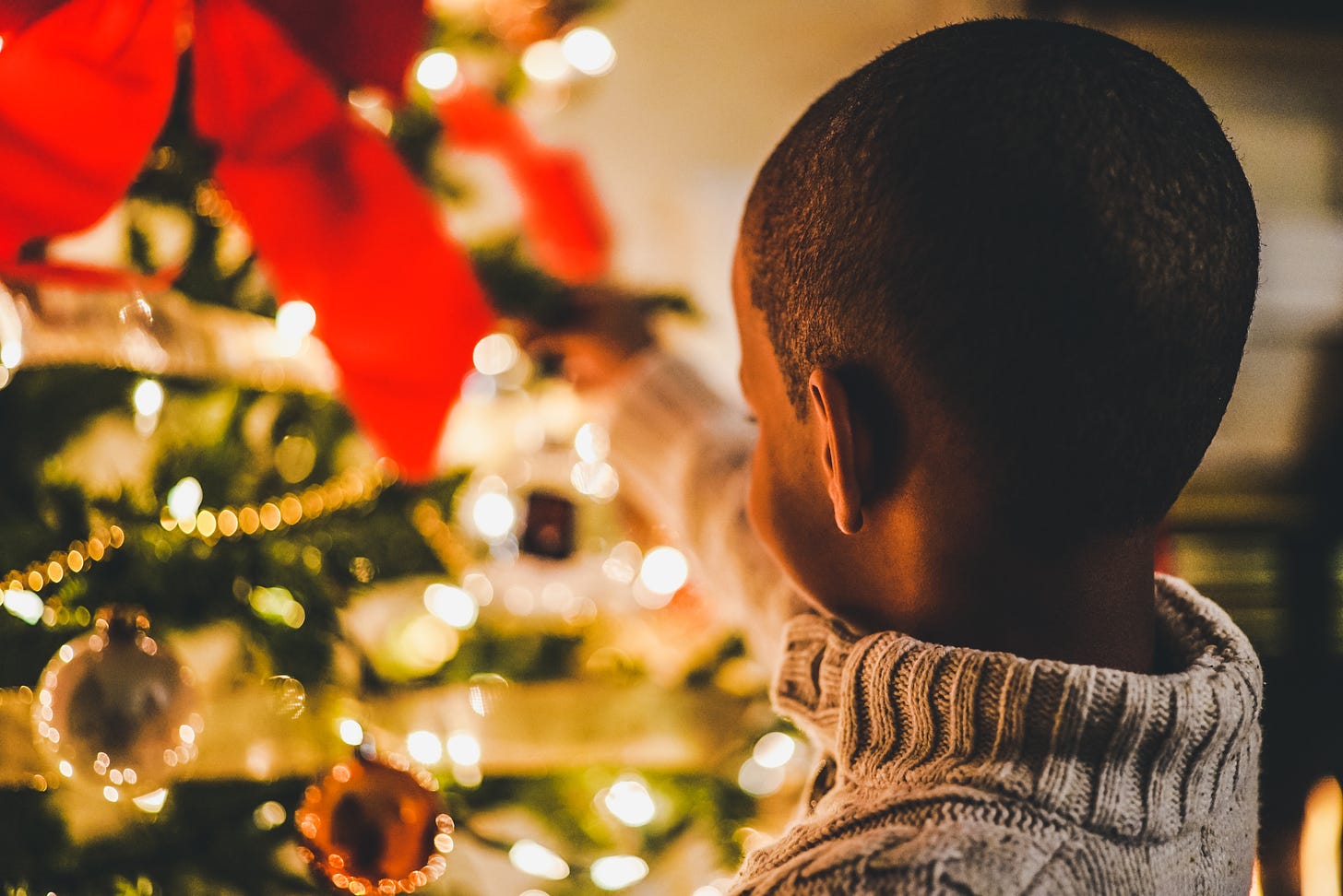A little boy with his back to the camera looks at a Christmas tree (Photo by Chris Benson on Unsplash)