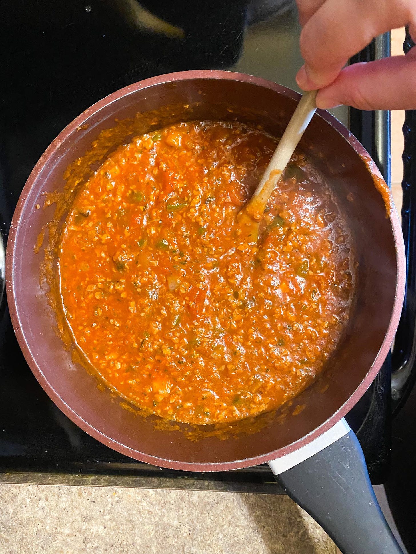 pasta sauce in a pot, a hand holding a wooden spoon, stirring