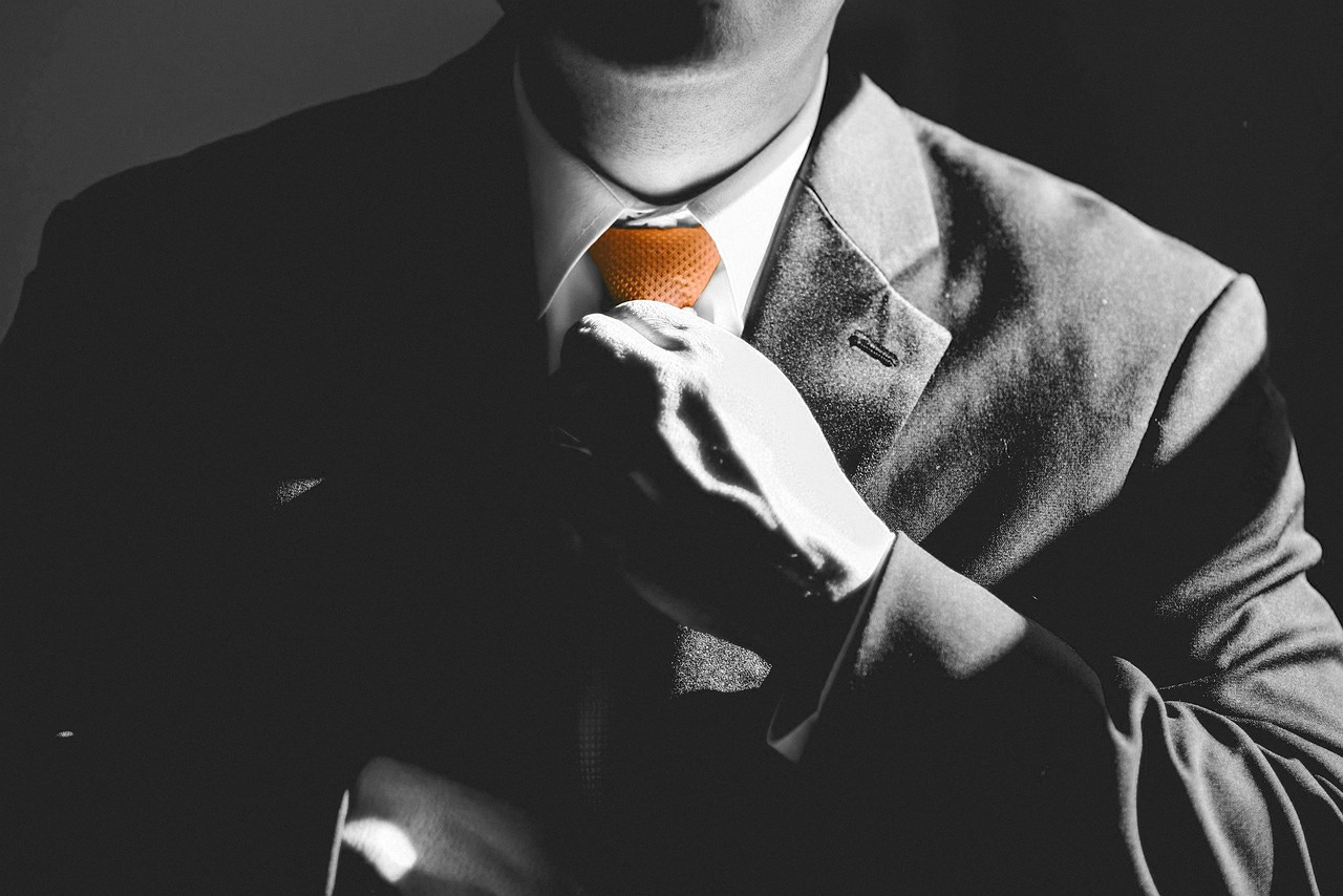 A man in a suit adjusts his tie. Black-and-white picture, but the tie is orange