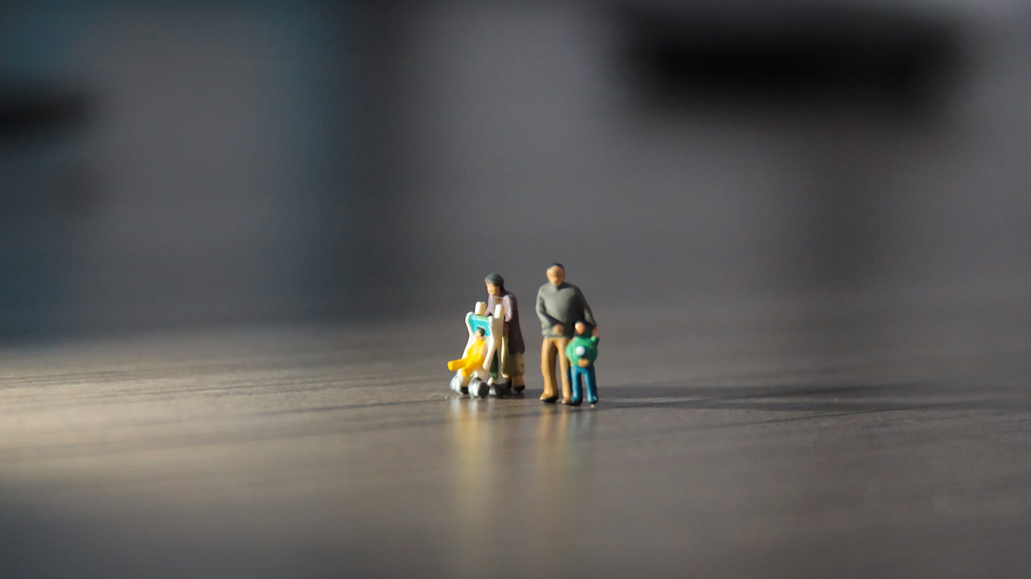 A small figurine family stands amid light and shadow.