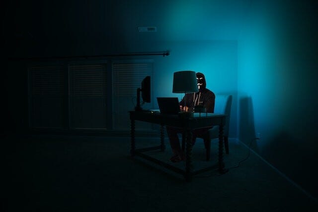 someone coding with a mask on in a dark room with a soft blue light