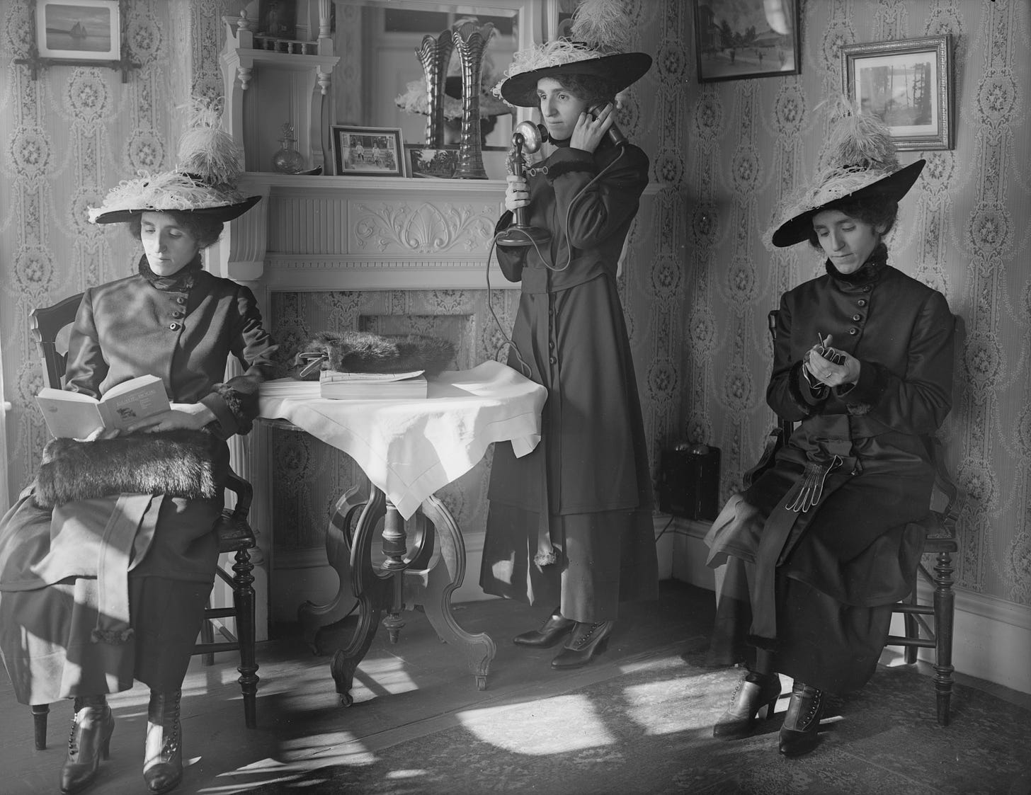 greyscale photo of three of the same women sitting, talking on the telephone, and reading