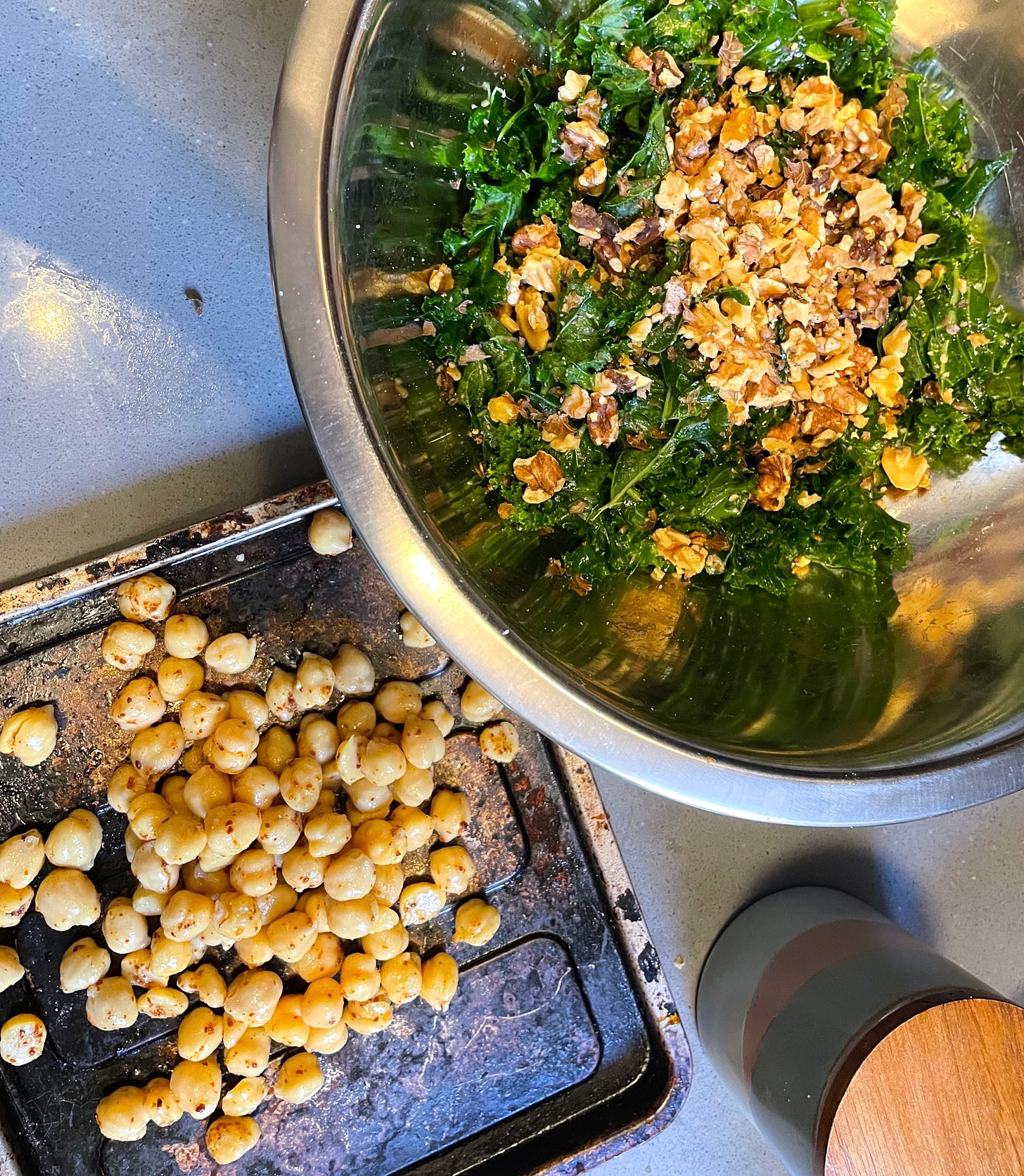 bowl of massaged kale and toasted walnuts next to seasoned chickpeas on tray