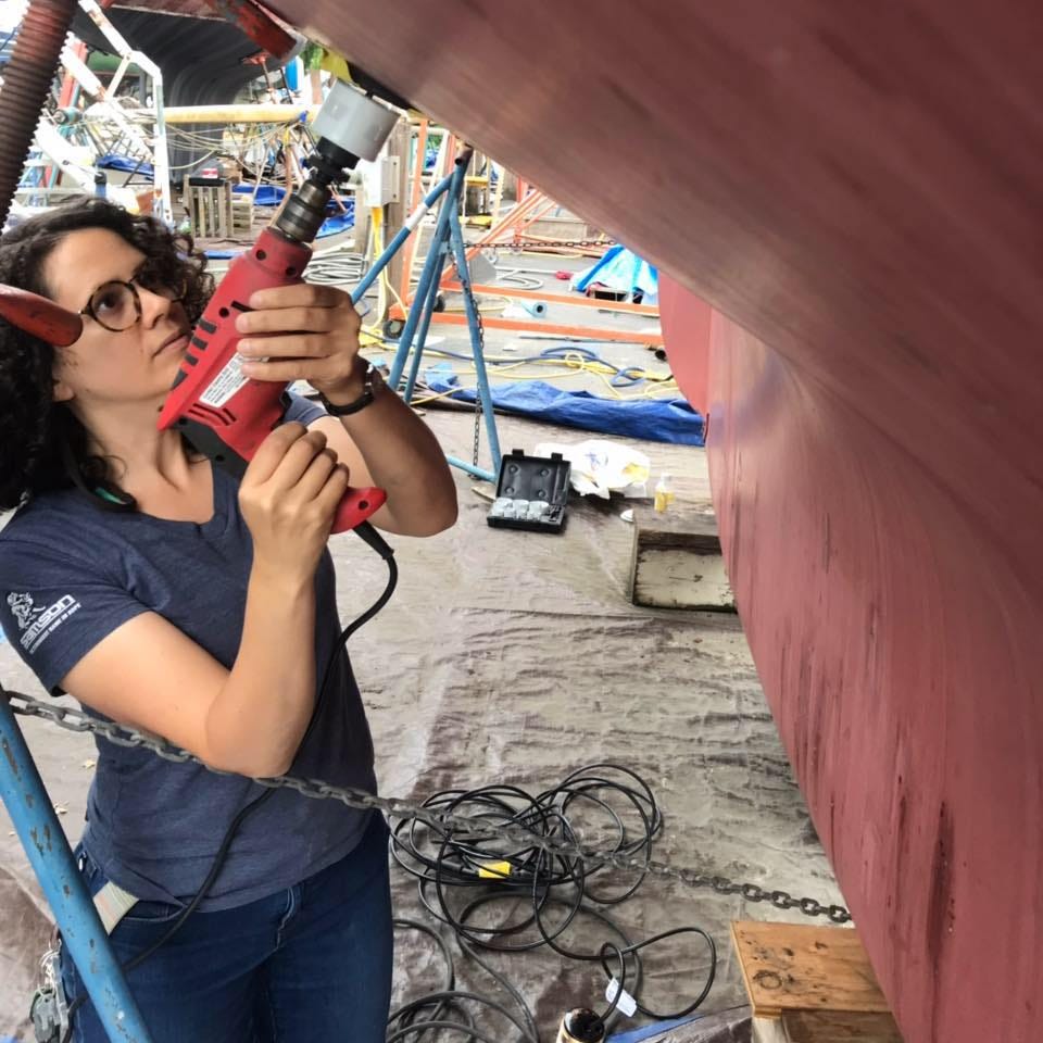 a woman drills a hole into a boat. 