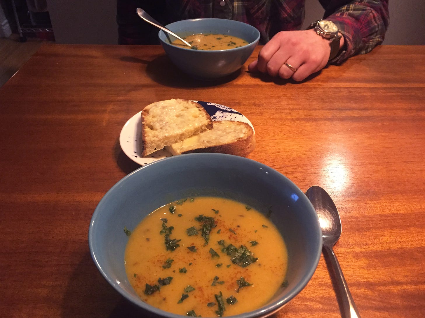 Two blue bowls across from each other on the table, each full of yellow lentil soup dusted with cilantro and chili powder. Between the two bowls is a plate with slices of cheesy toast.