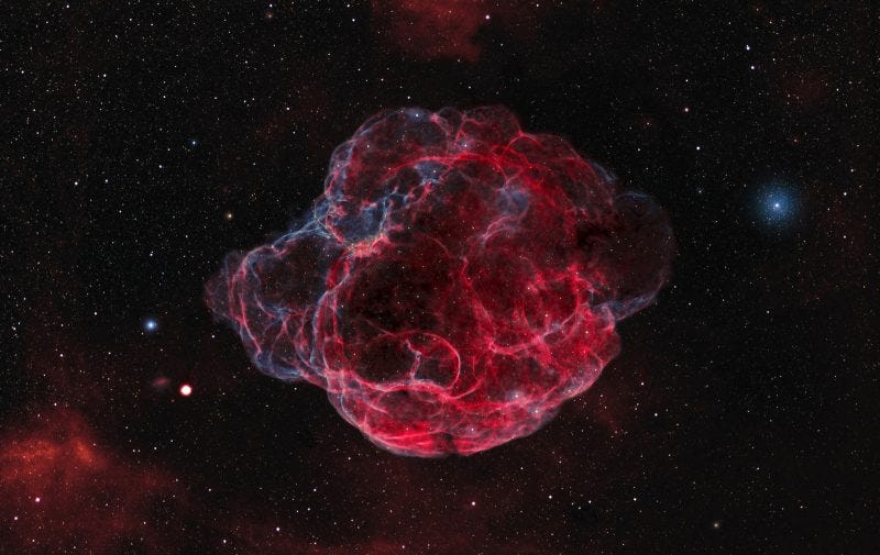 Red bulbous sphere of gas in deep sky with tinges of blue.