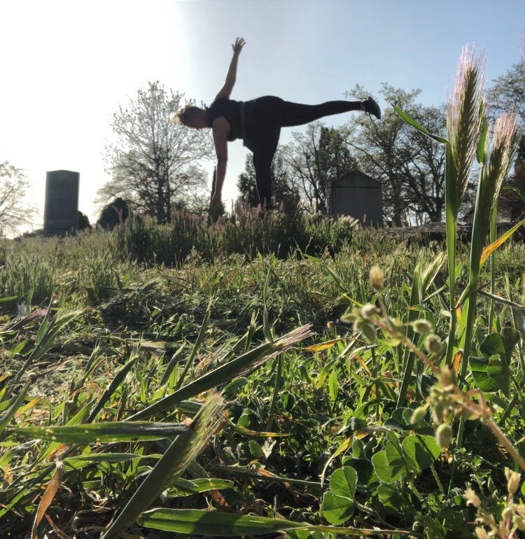 in the foreground, freshly mowed grass in shards. in the distance, a human in movement among gravestones under a clear blue sky