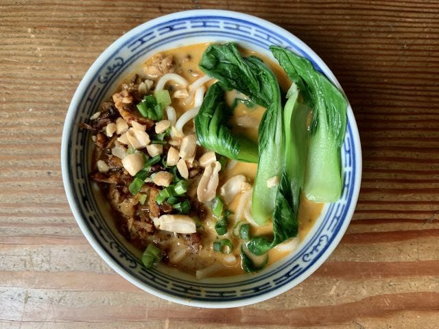 A bowl with noodles, peanuts, and bok choy floating in an orange broth
