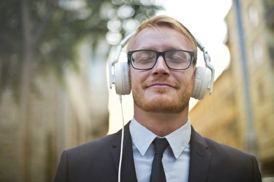 A businessman smiling and listening to an audio content with a headset