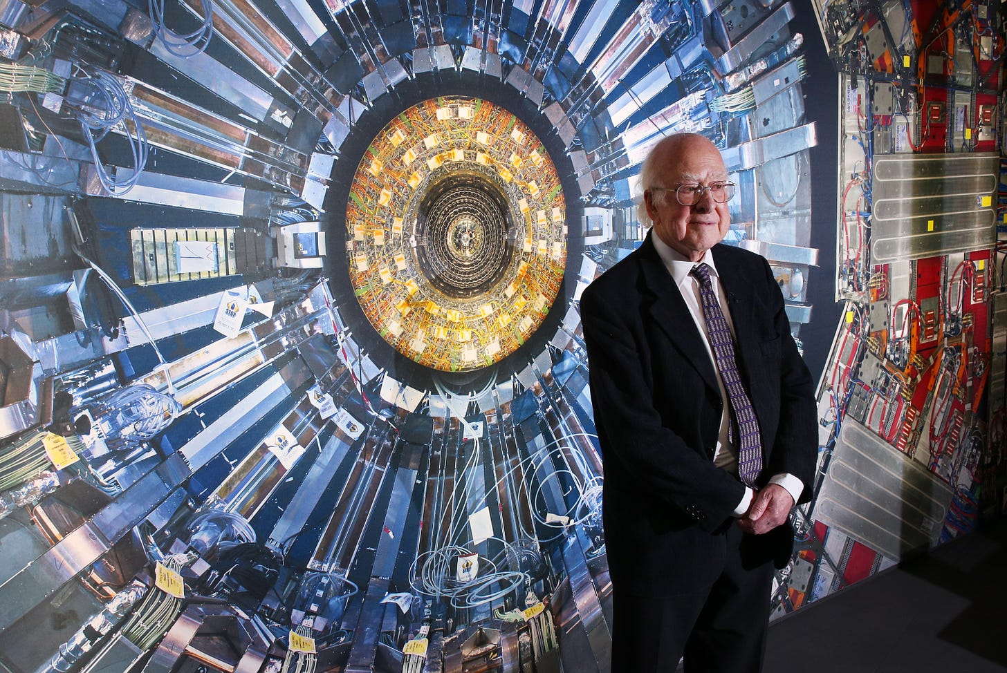 Mr. Peter Higgs in front of an image of one of the Large Hadron Colliders. Source: Photo by Peter Macdiarmid/Getty Images.