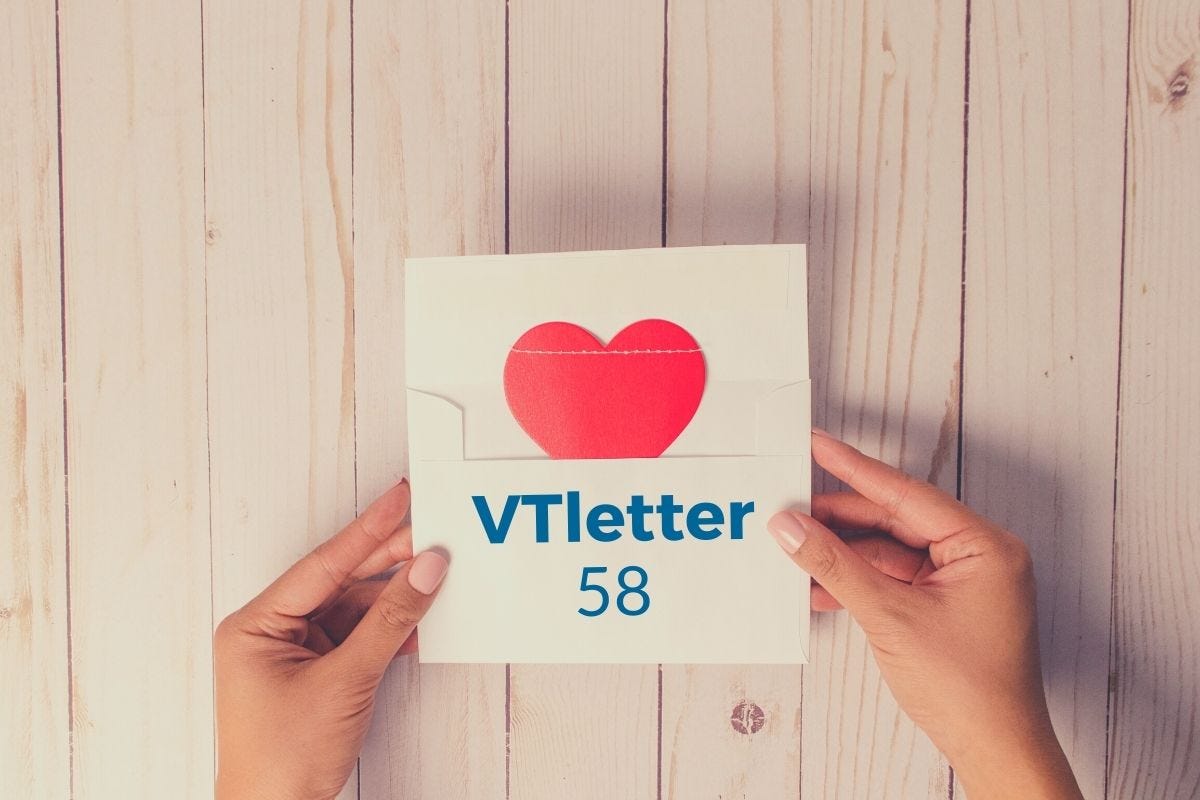 Mãos femininas sobre mesa de madeira segurando envelope aberto com carta contendo um coração e nome VTletter 58.