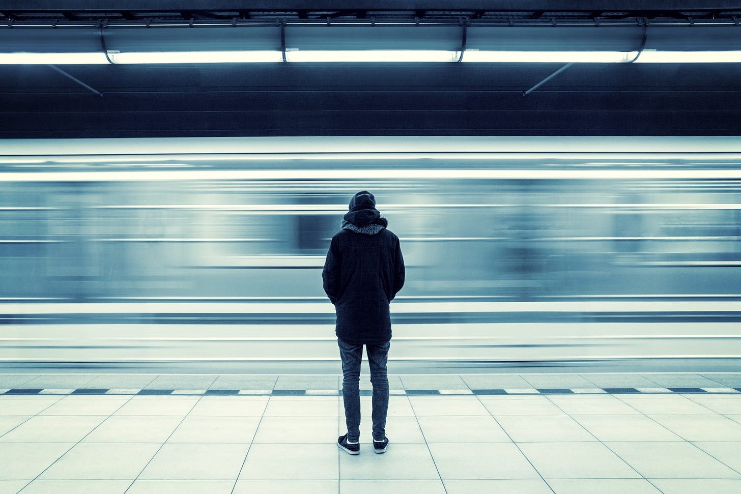 A person stands alone on a platform as a subway train whizzes by in a blur.