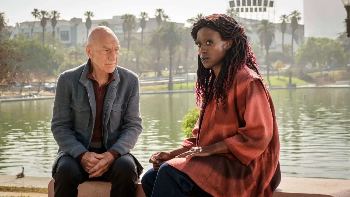 This image shows Jean-Luc Picard (played by Patrick Stewart) sitting on a park bench next to a younger version of his friend Guinan (played by Ito Aghayere) on a park bench in 2024 Los Angeles, California. Picard sits on the left and looks at Young Guinan, who sits on the right and looks into the middle distance. This image shows Jean-Luc Picard (played by Patrick Stewart) sitting on a park bench next to a younger version of his friend Guinan (played by Ito Aghayere) on a park bench in 2024 Los Angeles, California. Picard sits on the left and looks at Young Guinan, who sits on the right and looks into the middle distance.
