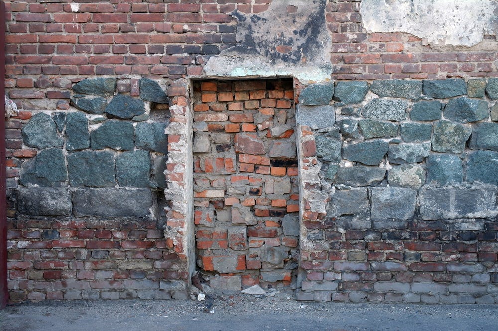 old wall of stone and red brick with a bricked up door