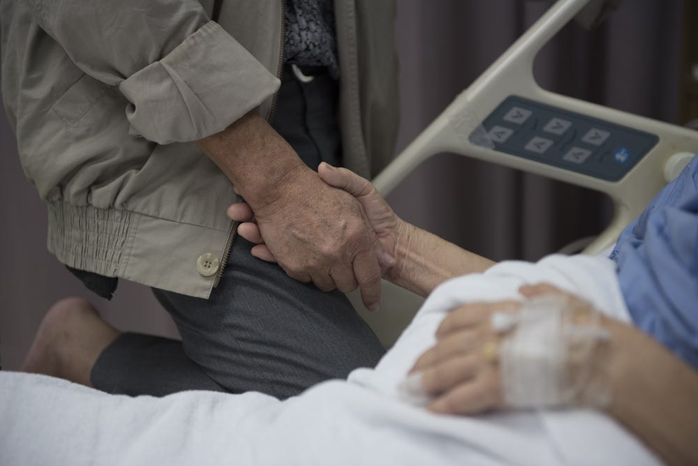 two people holding hands, one of whom is in a hospital bed. close cropped, so you see only hands and torsos