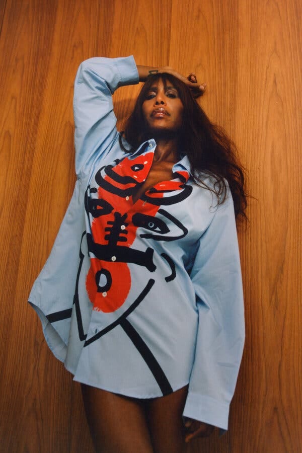 Honey Dijon wearing an oversize blue collared shirt with a red and black design on the front, and no pants.