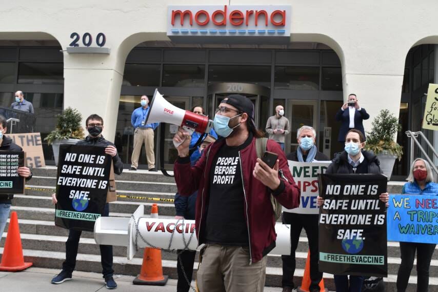 Masked man with bullhorn leads demonstration for vaccine equity infront of moderna lab