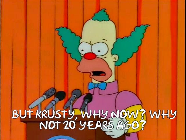 Krusty the Klown (from the Simpsons) behind a set of microphones at a press conference in front of an orange curtain. Caption (in Simpsons font) says "But Krusty, why now? Why not 20 years ago?"