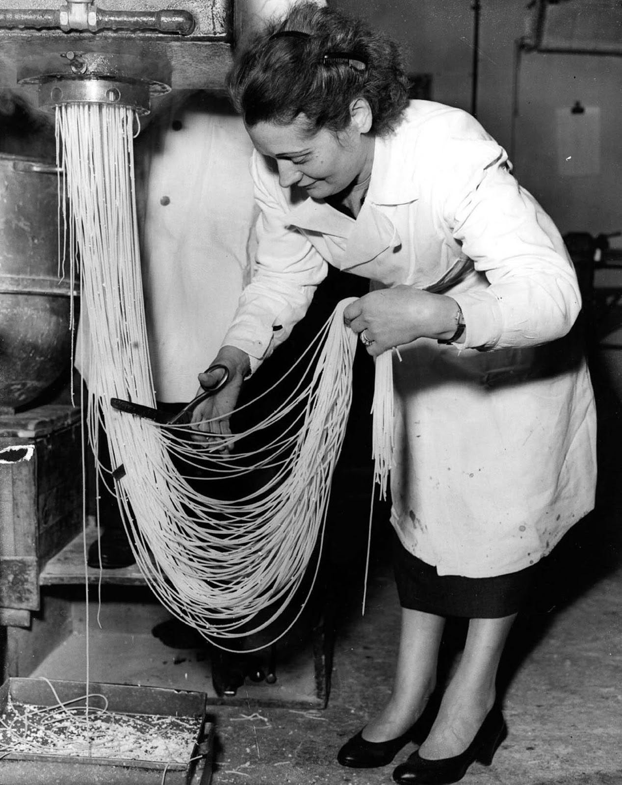 Zelda Albano cuts spaghetti into lengths as it emerges from a machine at a pasta factory in Holloway, London. 1955.