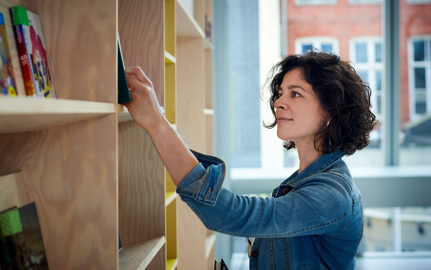 A woman searching through books on a shelf in a library