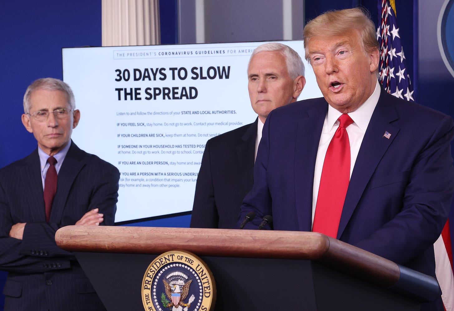 Dr. Anthony Fauci, Mike Pence, and Donald Trump stand in front of a graphic titled "30 DAYS TO SLOW THE SPREAD" on March 31, 2020