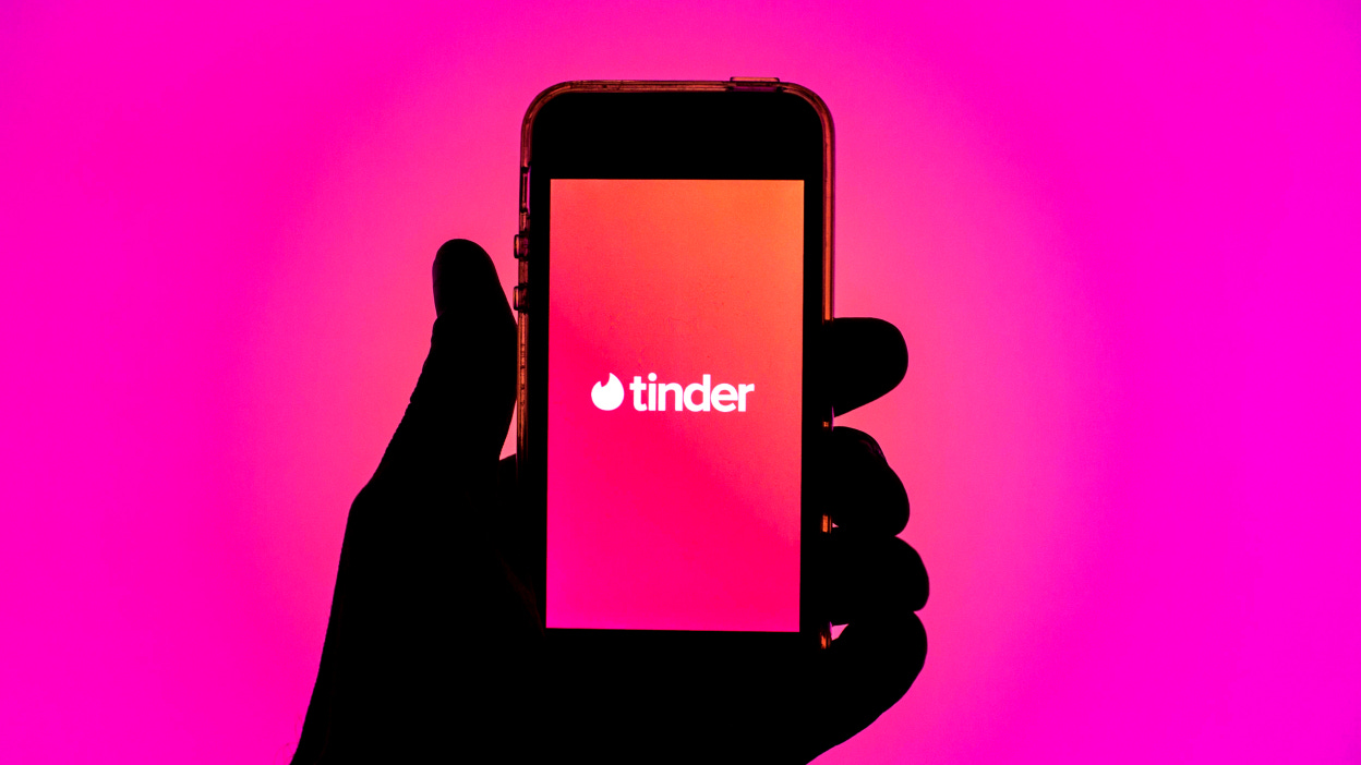 Tinder app seen displayed on a smartphone screen in front of pink background