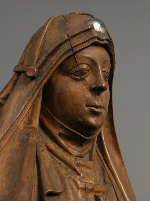 Närbild av en träskulptur: man ser en kvinnas huvud med dok på huvudet. På doket syns den korskrans som birgittasystrarna bär.